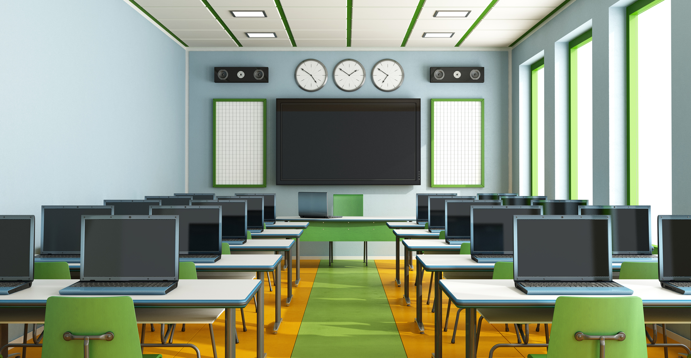 Bright computer training classroom with rows of laptops, green chairs, large wall display flanked by clocks and speakers, and floor-to-ceiling windows on the right.