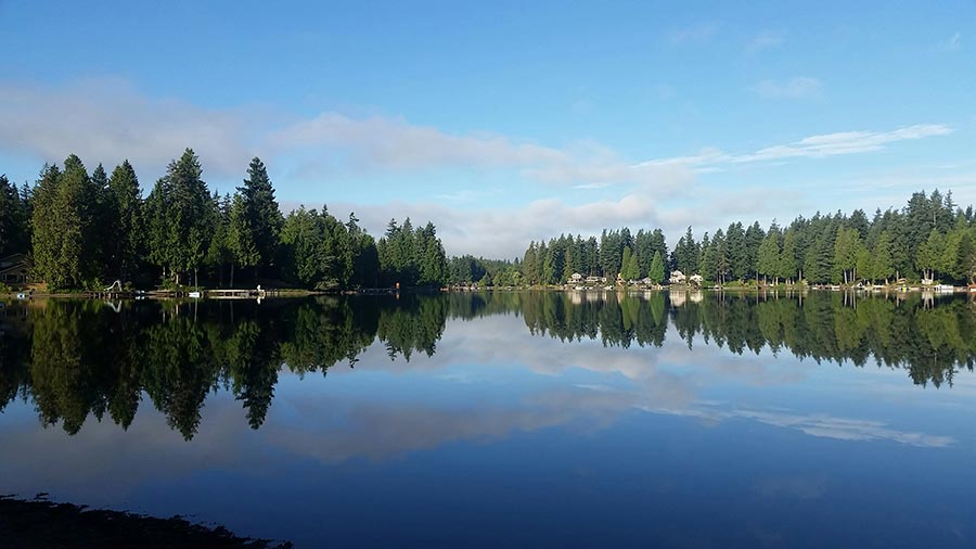 Calm lake reflecting evergreen trees and a blue sky with light clouds