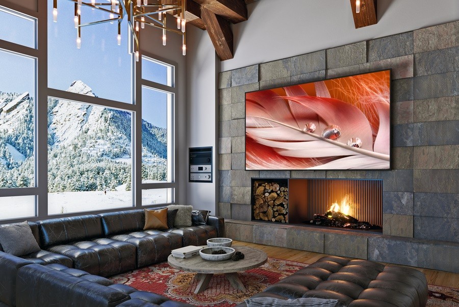 A large Sony flat-screen TV above a lit fireplace in a living room with picture windows looking out over the mountains.