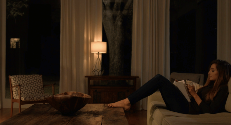 A woman relaxing omn the couch in the living room with the lights a warm orange color.