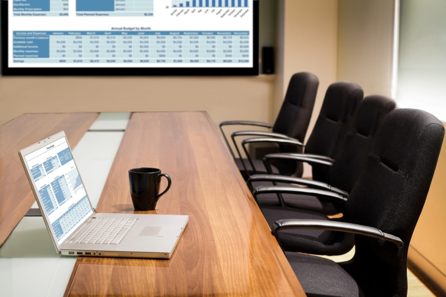 A laptop sits on a table in a conference room. 