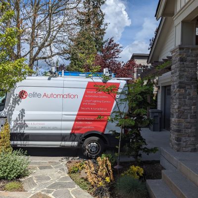 An Elite Automation service van parked in a driveway, surrounded by landscaped shrubs and trees in a residential setting.