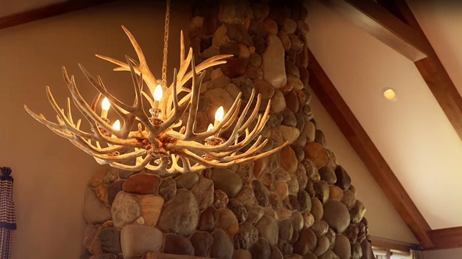 Antler chandelier with warm lighting in rustic stone fireplace room