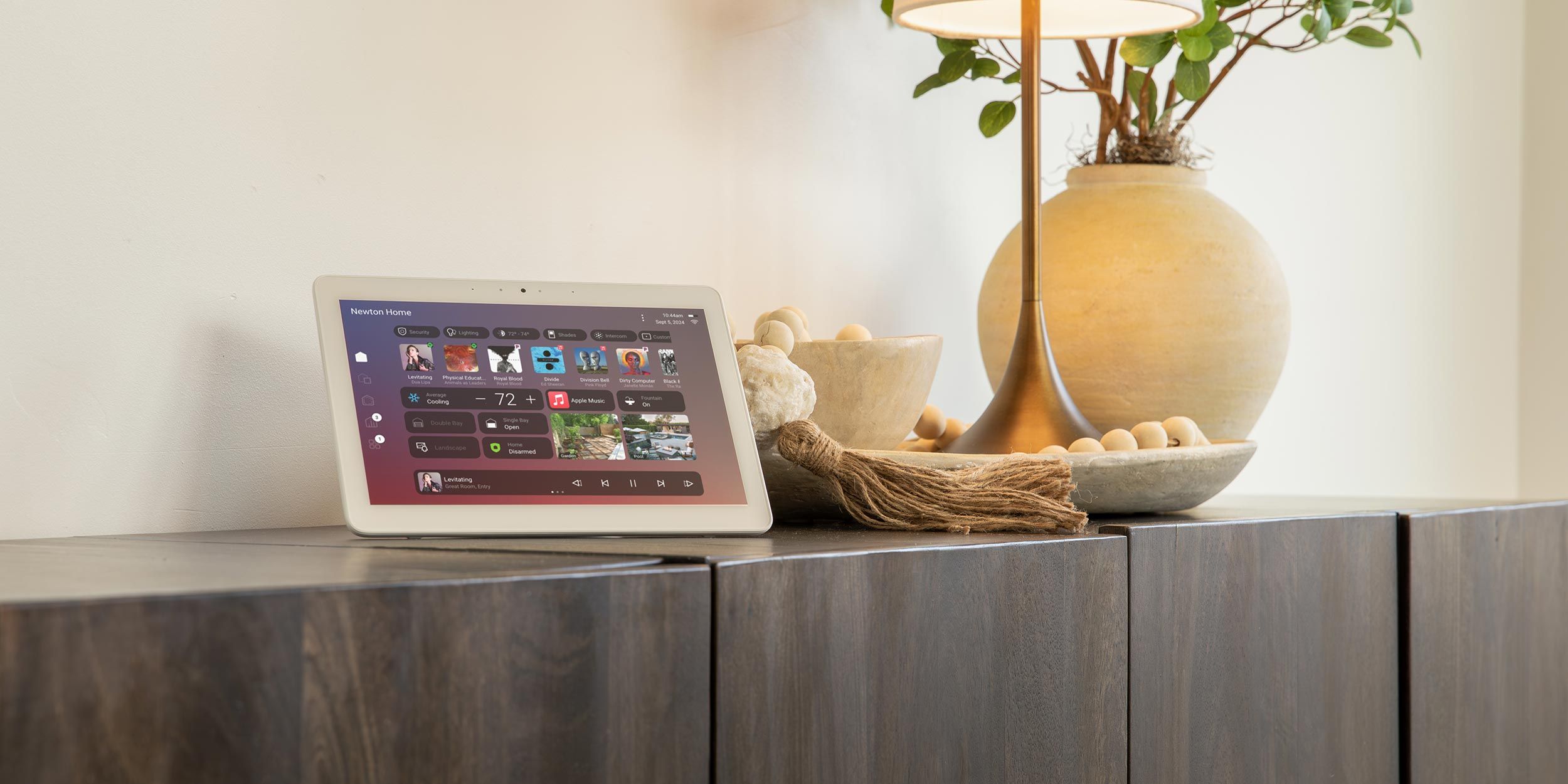 Smart home tablet displaying control interface on wooden cabinet near lamp