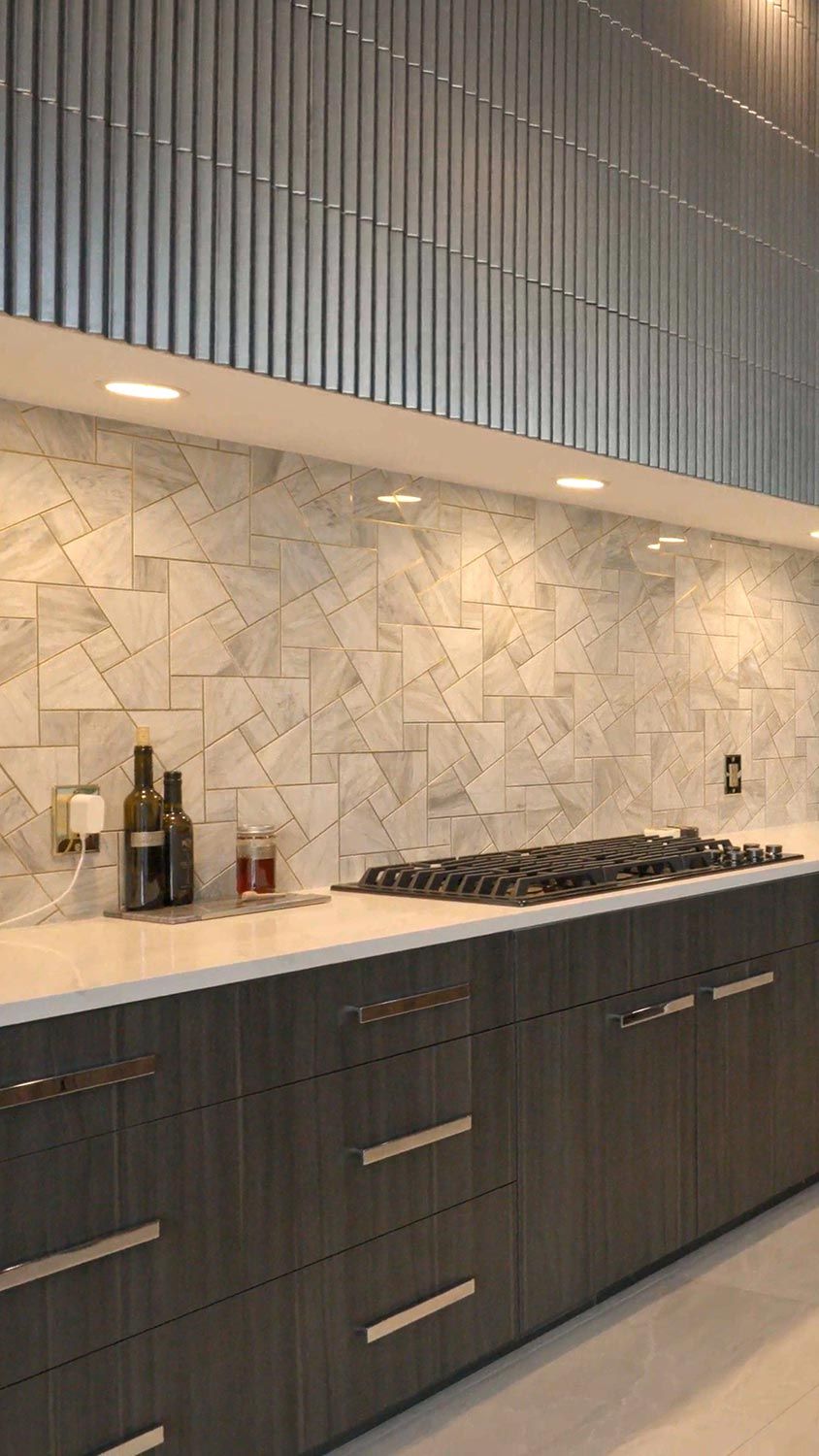A modern kitchen with dark wood cabinets, a light-colored marble backsplash, and integrated lighting.