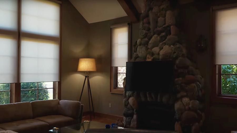 Living room with stone fireplace and automated window shades partially lowered
